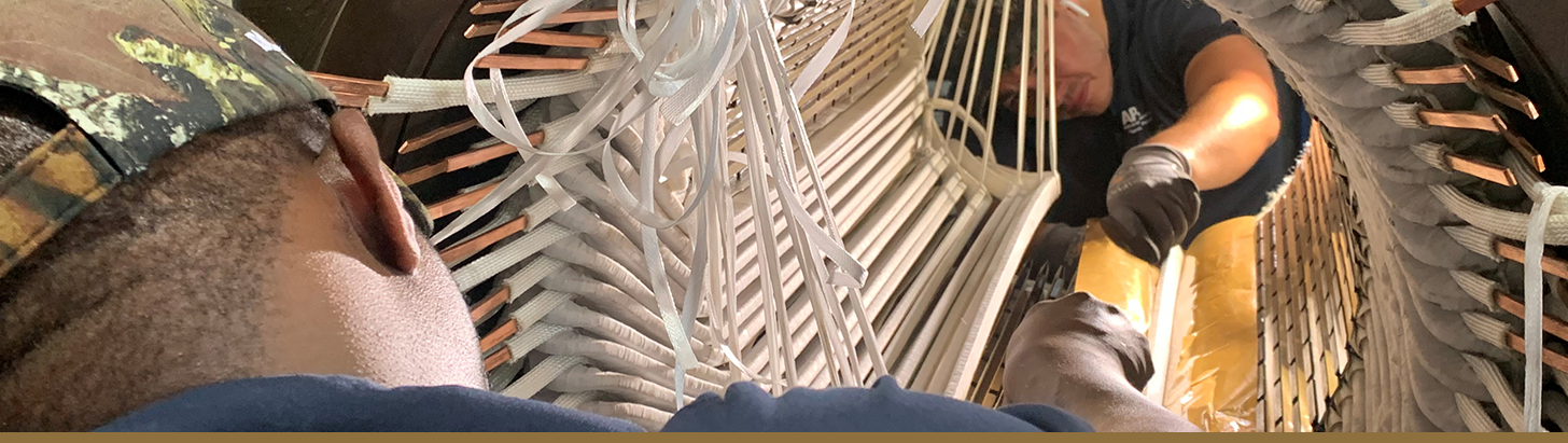 Over-the-shoulder view of two winding technicians at Apex Industrial Automation repairing a large AC/DC electric motor, focusing on the intricate motor rewind process.