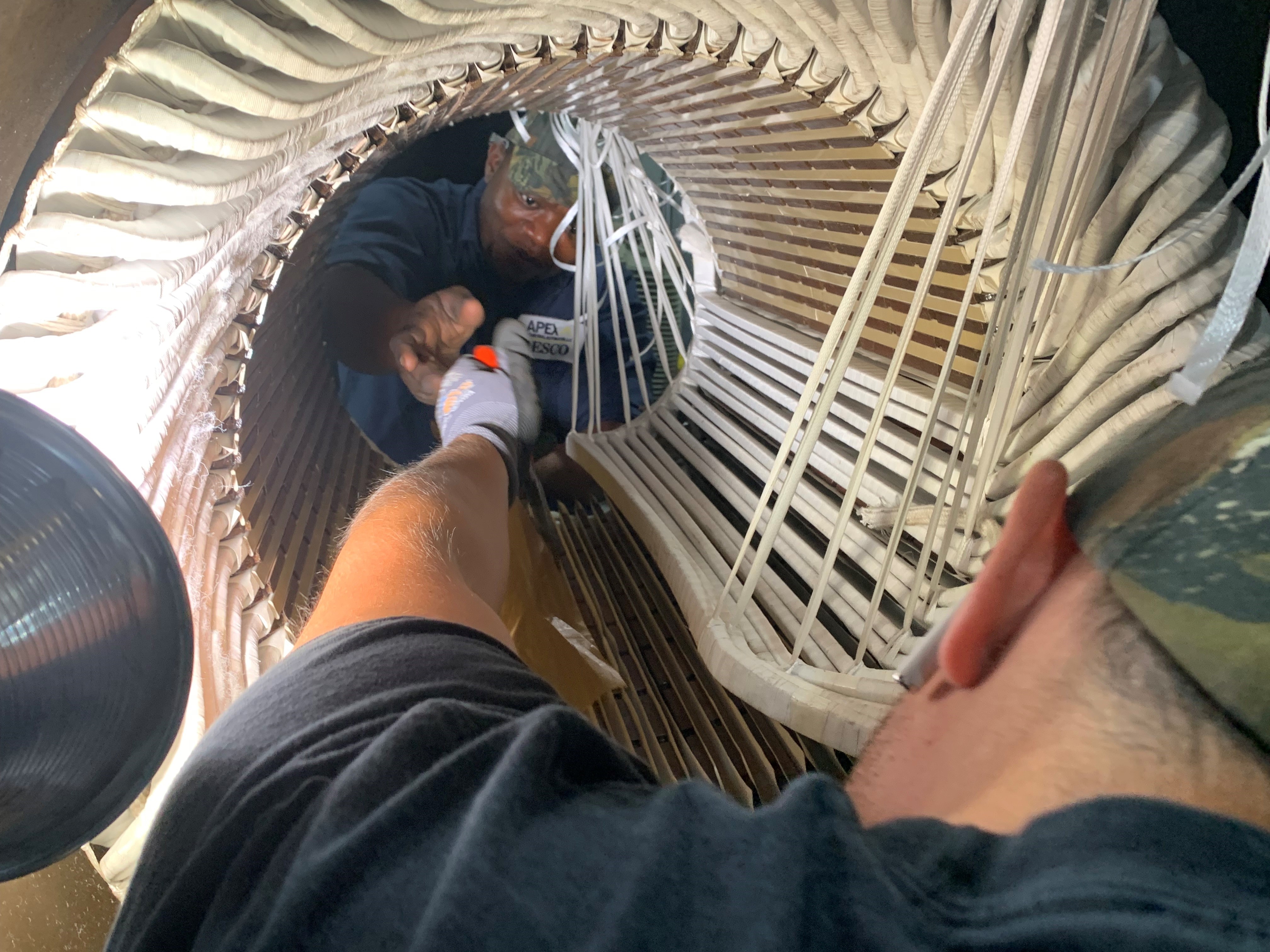 Two technicians at Apex Industrial Automation collaboratively working on a motor rewind, exchanging tools through the center of the motor stator.
