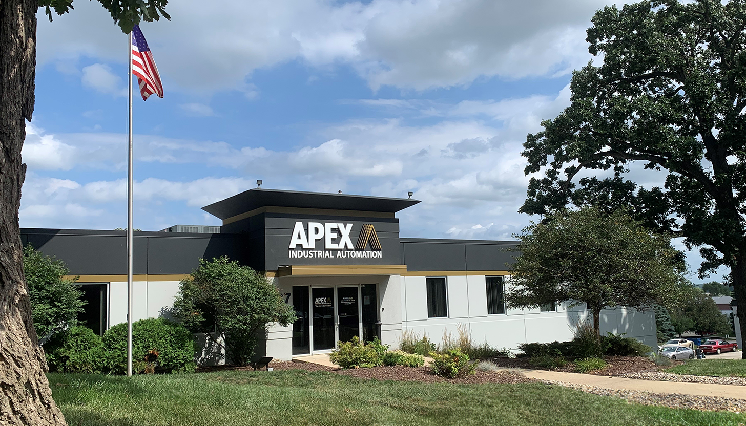 Exterior view of the Apex Industrial Automation main headquarters in northern Illinois, featuring the company logo on the building painted in company colors, with lush green grass and a cloudy blue sky.