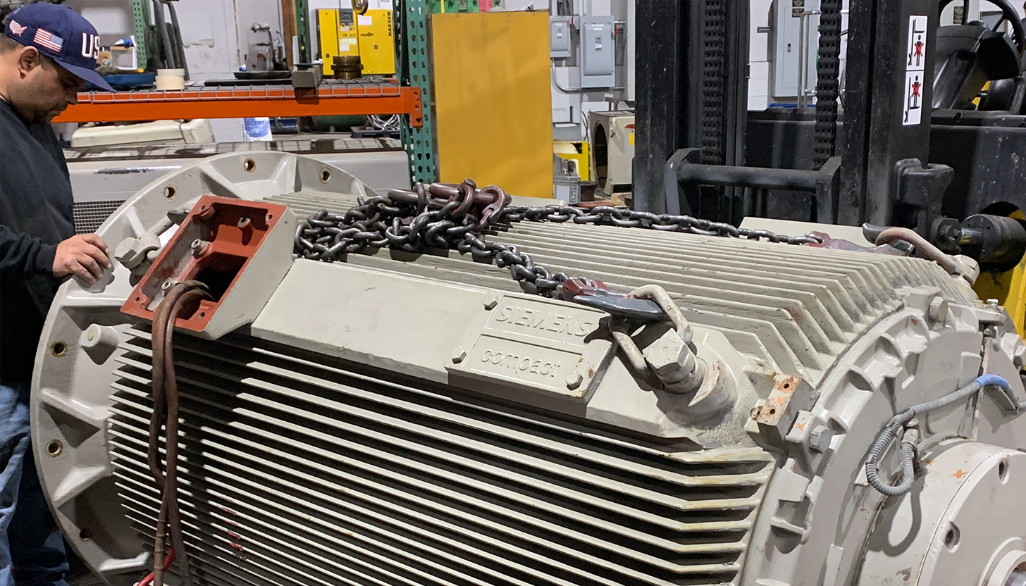 Apex Industrial Automation technician working on a large AC/DC electric motor repair, with chains draped over it from recent crane operations.