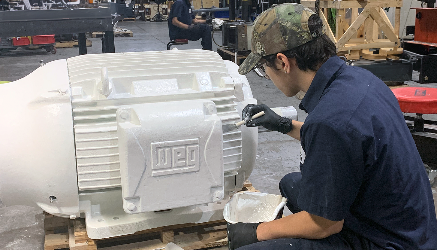 Repair technician at Apex Industrial Automation painting a repaired WEG electric motor, preparing it for delivery.