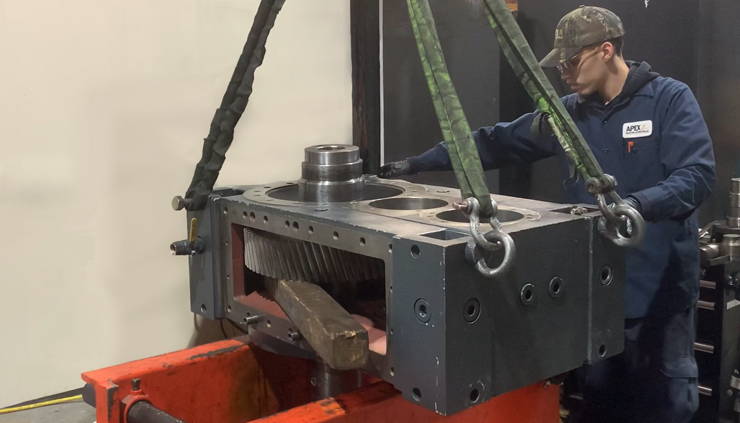 Gearbox repair mechanic at Apex Industrial Automation positioning a large industrial gearbox onto a repair table, assisted by a large crane.