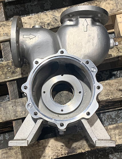 Center-frame disassembled industrial pump housing with intake and output pipes on a wooden pallet, awaiting pump repair at Apex Industrial Automation.