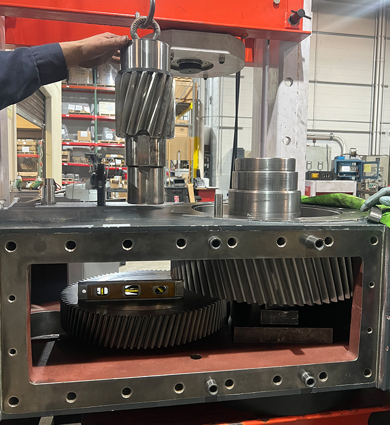 Side view of a large gearbox being disassembled at Apex Industrial Automation, with a crane lifting a gear cylinder from the housing.