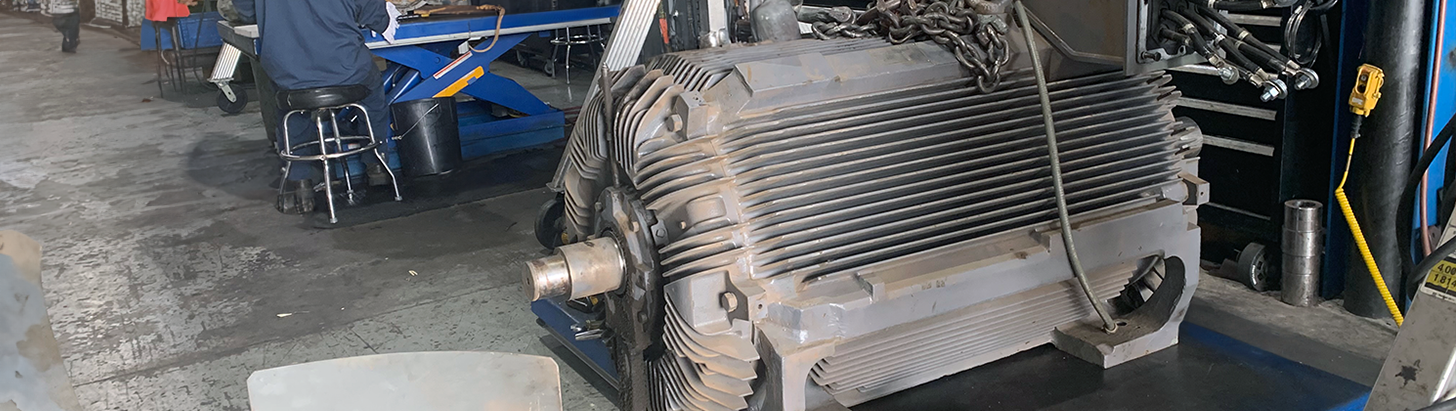 Large AC electric motor on a lift workbench at Apex Industrial Automation’s repair center, with a technician working in the background.