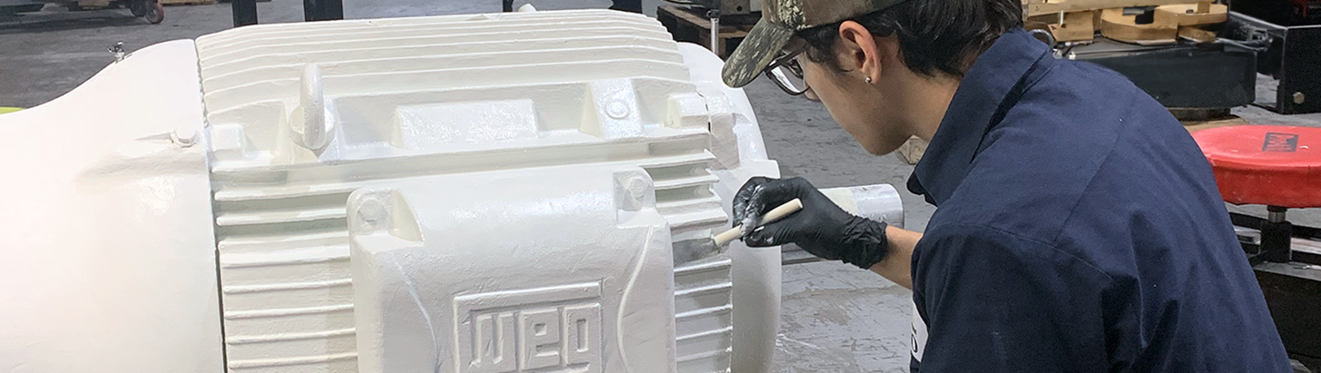 Repair technician at Apex Industrial Automation painting a large AC WEG motor white after completing repairs.