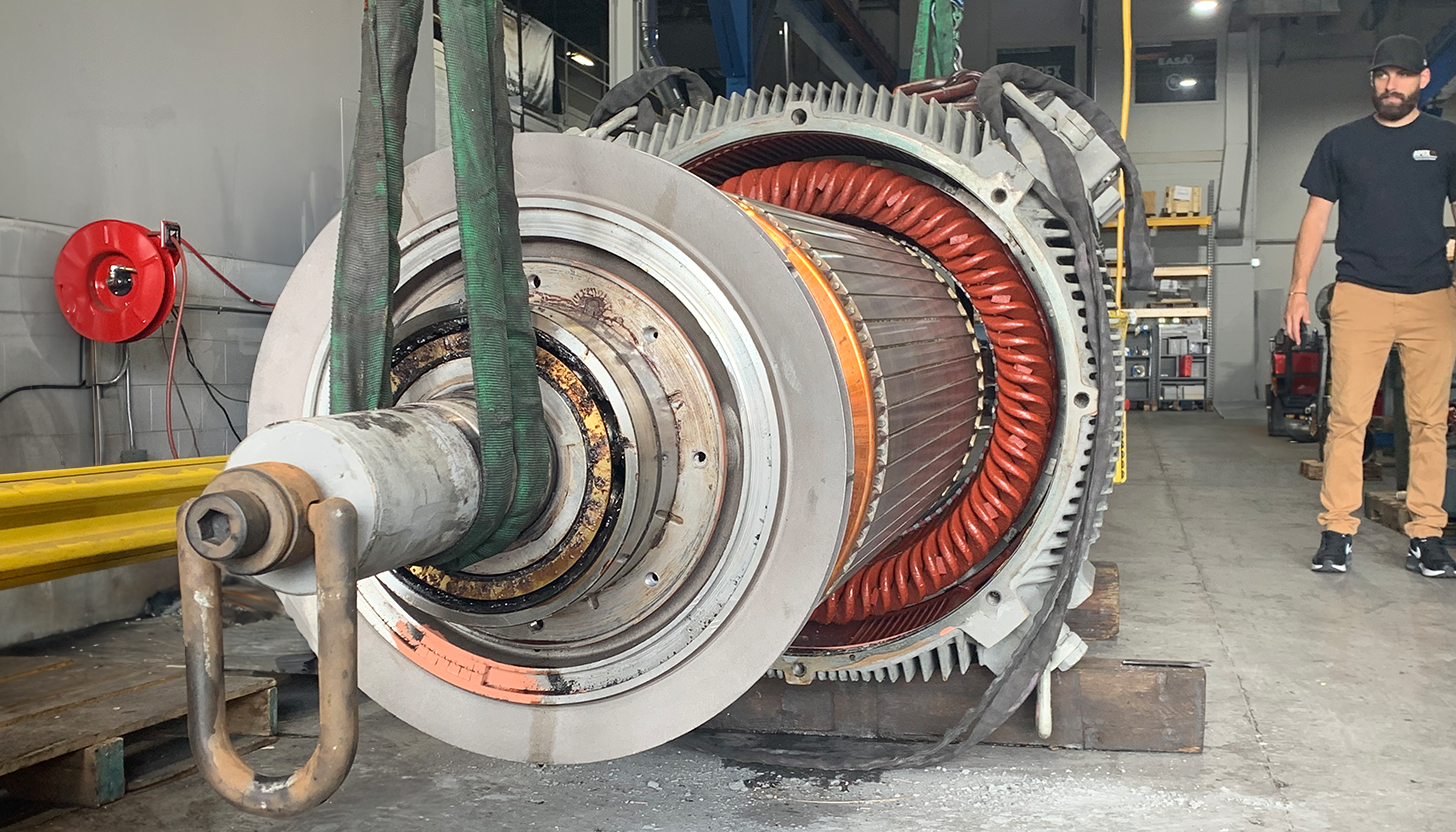 Large electric motor disassembly at Apex Industrial Automation, with the rotor halfway out and supported by a crane.